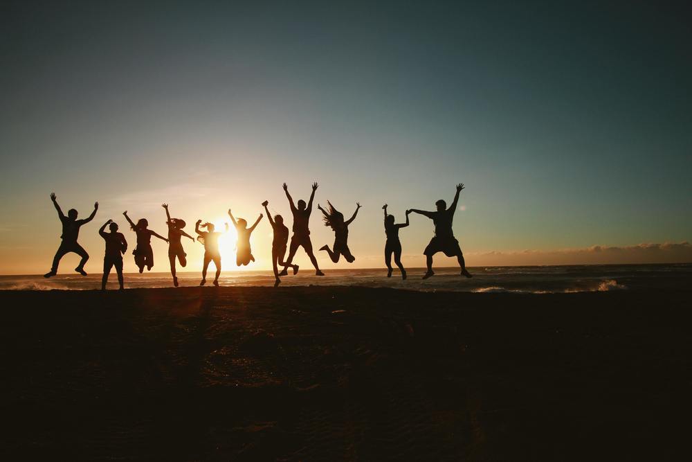 silhouette of 10 people jumping on a beach in front of sunset